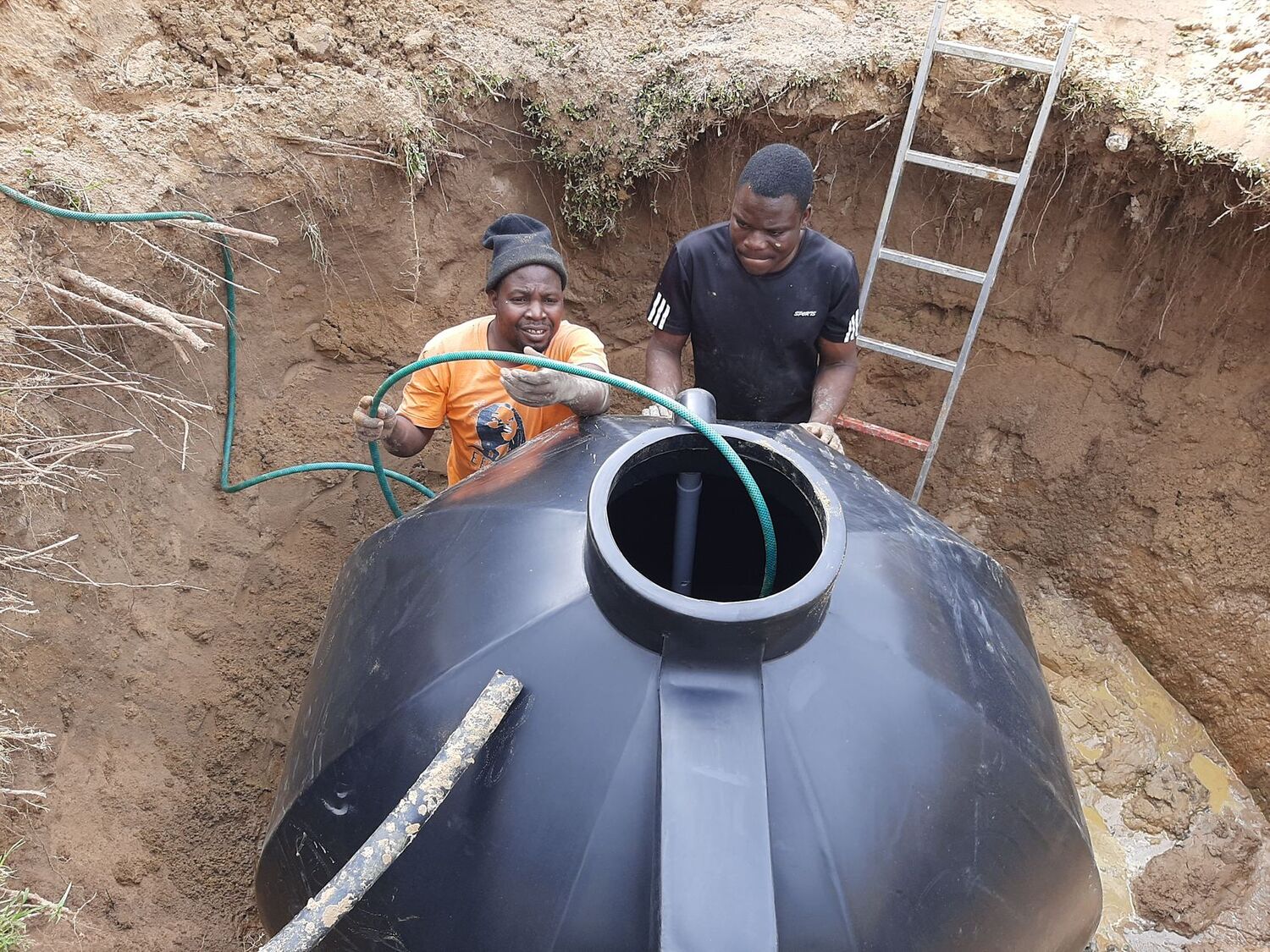 Two H2O Systems installers fitting an underground storage tank in an excavated pit.